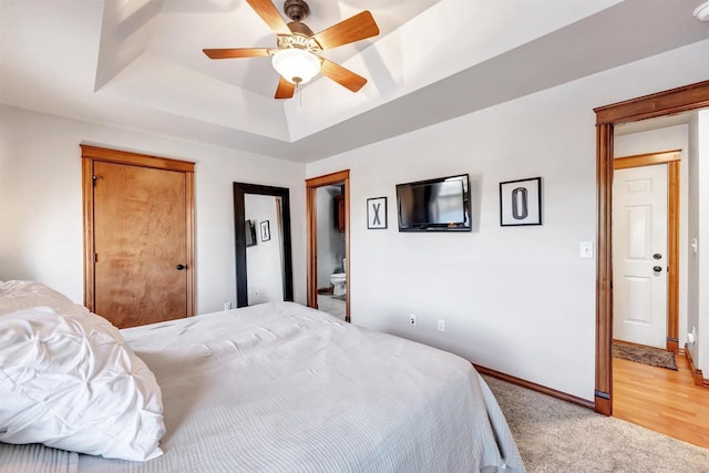 bedroom with ceiling fan, light carpet, a tray ceiling, and connected bathroom