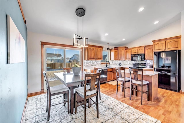 dining room featuring sink, light hardwood / wood-style flooring, and vaulted ceiling