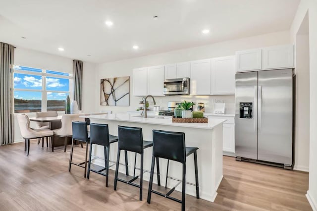 kitchen with white cabinets, a kitchen island with sink, stainless steel appliances, and light hardwood / wood-style floors