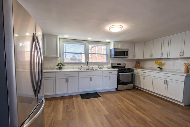 kitchen featuring wood-type flooring, sink, light stone countertops, stainless steel appliances, and white cabinets