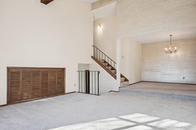 unfurnished living room with light colored carpet, beam ceiling, a towering ceiling, and a notable chandelier