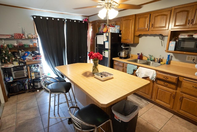 kitchen with sink, stainless steel fridge, ceiling fan, light tile patterned floors, and a breakfast bar area