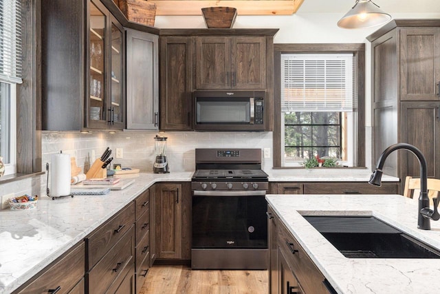 kitchen with decorative light fixtures, sink, appliances with stainless steel finishes, dark brown cabinets, and light stone counters