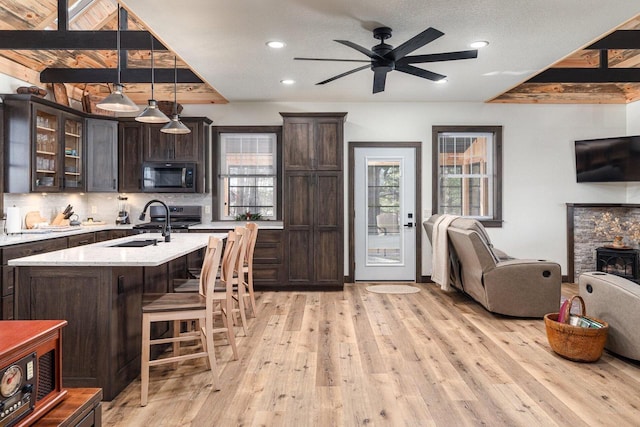 kitchen with light stone counters, hanging light fixtures, dark brown cabinetry, and stainless steel appliances