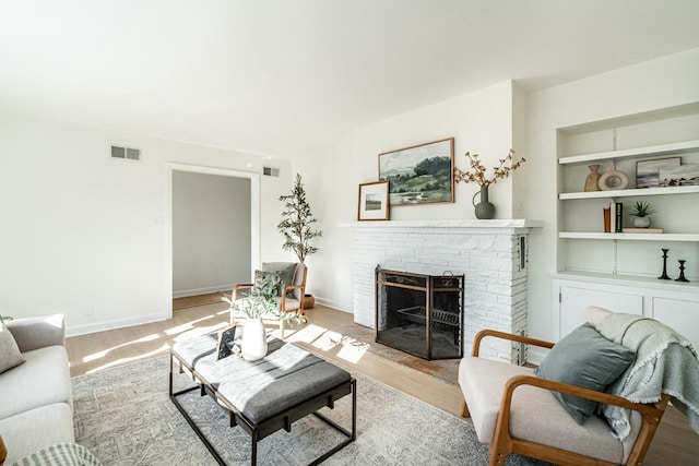 living room with built in features, a fireplace, and light hardwood / wood-style flooring