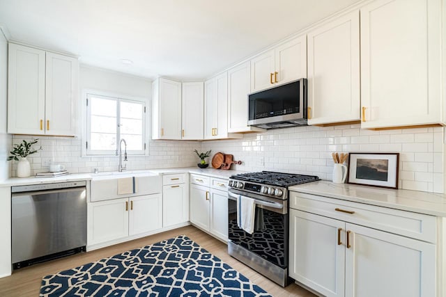 kitchen featuring sink, white cabinetry, stainless steel appliances, light hardwood / wood-style floors, and decorative backsplash