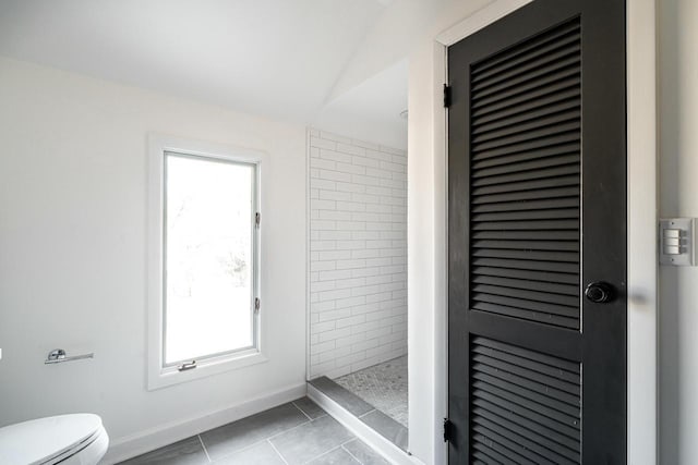 bathroom featuring tiled shower, toilet, and tile patterned flooring