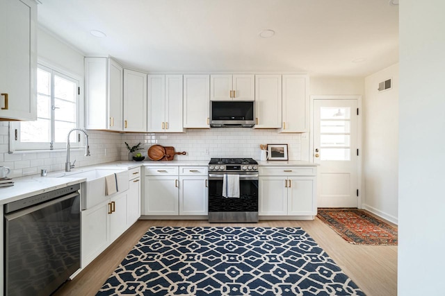 kitchen with sink, appliances with stainless steel finishes, backsplash, white cabinets, and light wood-type flooring