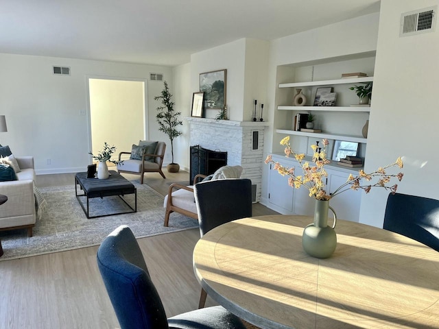 dining space with built in shelves, a fireplace, and light hardwood / wood-style floors