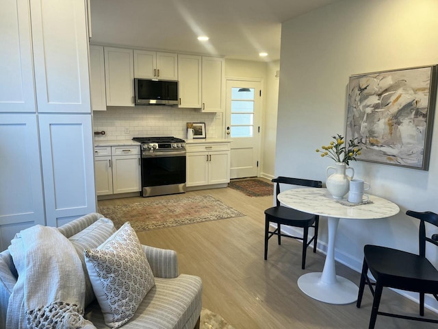 kitchen featuring tasteful backsplash, light hardwood / wood-style floors, white cabinets, and appliances with stainless steel finishes