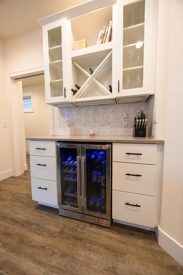 bar with beverage cooler, baseboards, a bar, dark wood finished floors, and tasteful backsplash