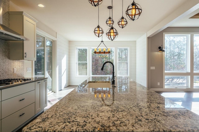 kitchen with stainless steel gas cooktop, a wealth of natural light, stone countertops, a sink, and wall chimney exhaust hood