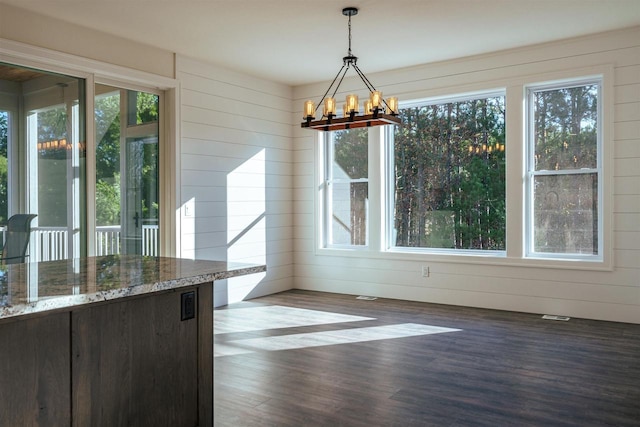 unfurnished dining area featuring a healthy amount of sunlight, wooden walls, a chandelier, and wood finished floors