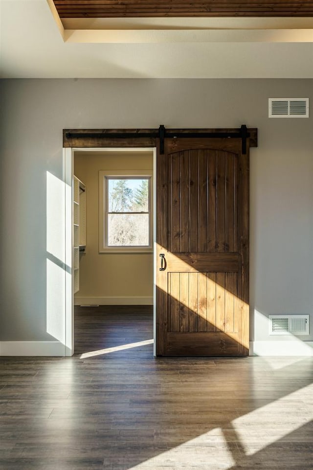 empty room with a barn door, wood finished floors, and visible vents