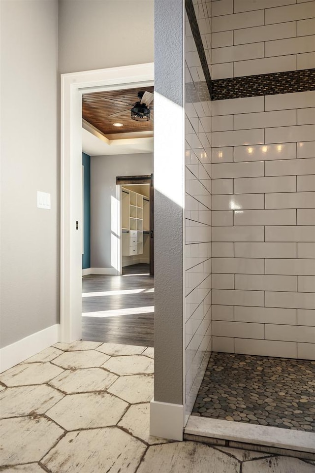 bathroom featuring a raised ceiling, a tile shower, and baseboards