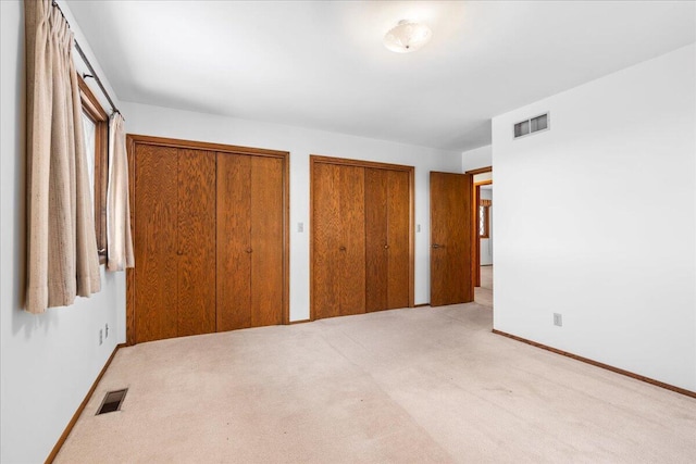 unfurnished bedroom with two closets and light colored carpet