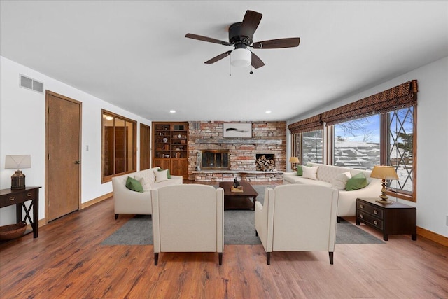 living room with ceiling fan, built in features, hardwood / wood-style flooring, and a stone fireplace