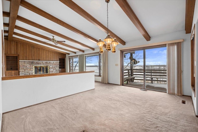 unfurnished living room with light colored carpet, lofted ceiling with beams, ceiling fan with notable chandelier, and a stone fireplace