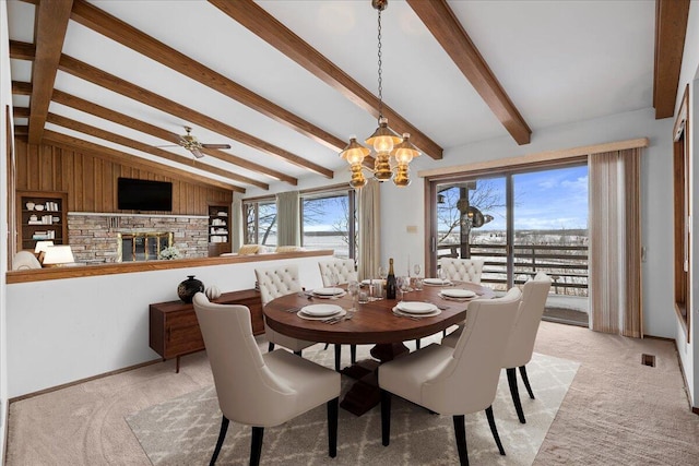 dining space featuring a fireplace, lofted ceiling with beams, wooden walls, light carpet, and ceiling fan with notable chandelier