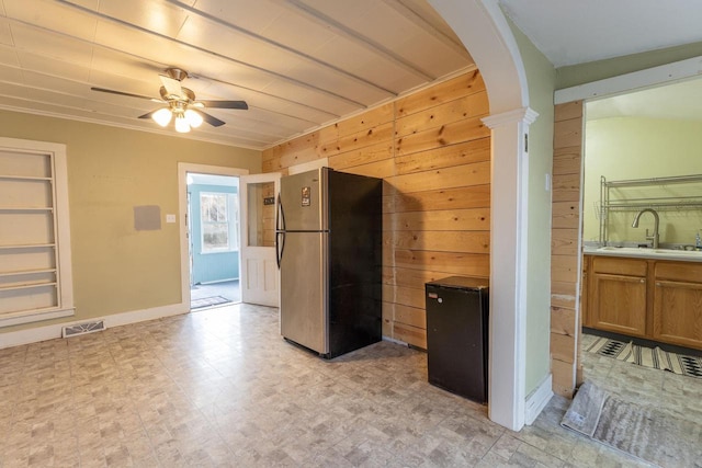 kitchen with sink, stainless steel fridge, ceiling fan, wooden walls, and ornate columns