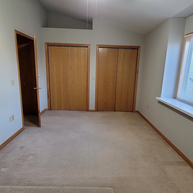 unfurnished bedroom with multiple closets, light carpet, and vaulted ceiling