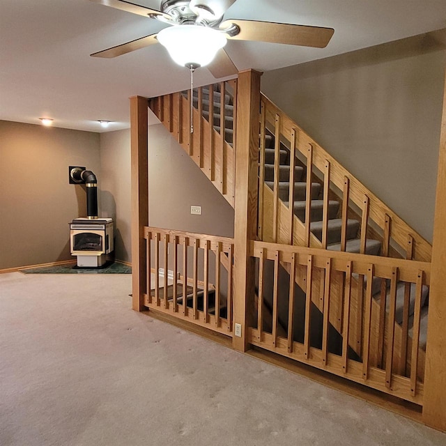 stairway featuring ceiling fan, a wood stove, and carpet floors