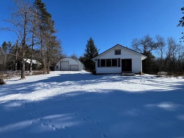 snow covered rear of property with a garage and an outbuilding