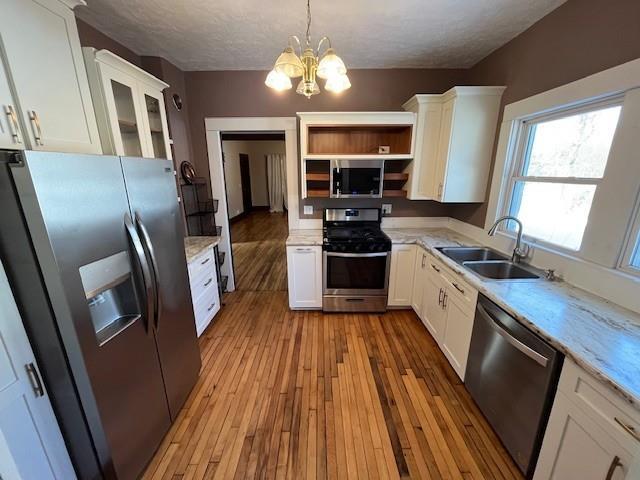 kitchen with a notable chandelier, pendant lighting, sink, white cabinetry, and appliances with stainless steel finishes