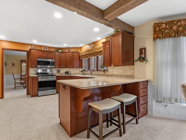 kitchen with a kitchen bar, kitchen peninsula, appliances with stainless steel finishes, backsplash, and beamed ceiling