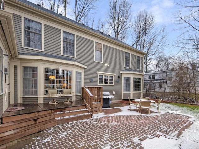 snow covered house featuring a patio area and a wooden deck