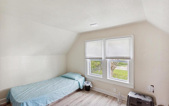 bedroom with hardwood / wood-style flooring, a textured ceiling, and vaulted ceiling