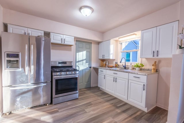 kitchen featuring white cabinetry, stainless steel appliances, light hardwood / wood-style floors, sink, and light stone counters