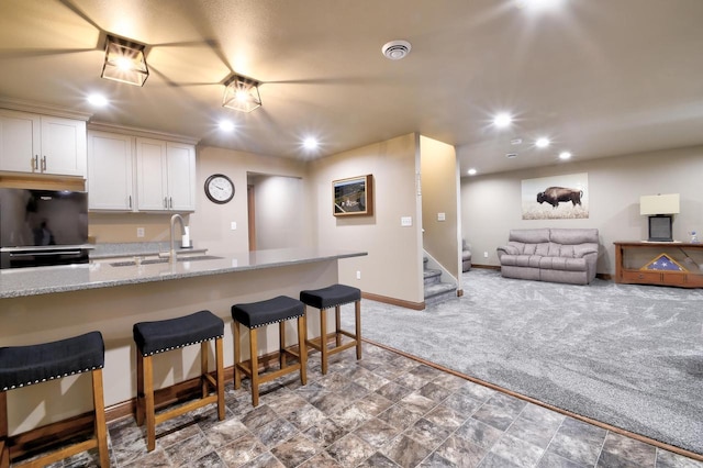 kitchen with black refrigerator, a kitchen breakfast bar, white cabinets, light stone counters, and sink