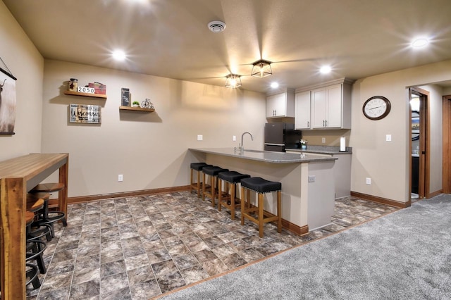 kitchen featuring black fridge, a kitchen bar, kitchen peninsula, white cabinetry, and carpet flooring