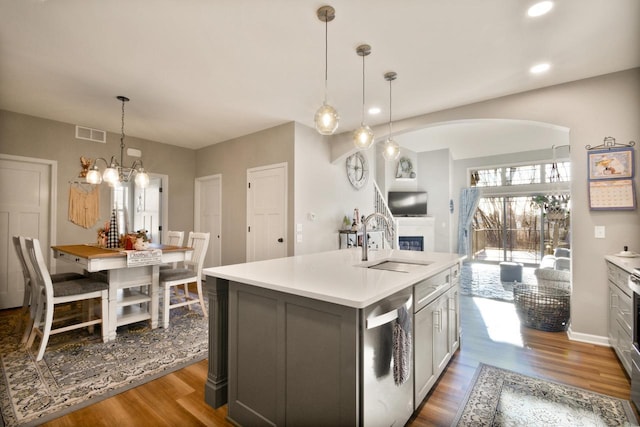 kitchen featuring pendant lighting, dishwasher, wood-type flooring, sink, and a center island with sink