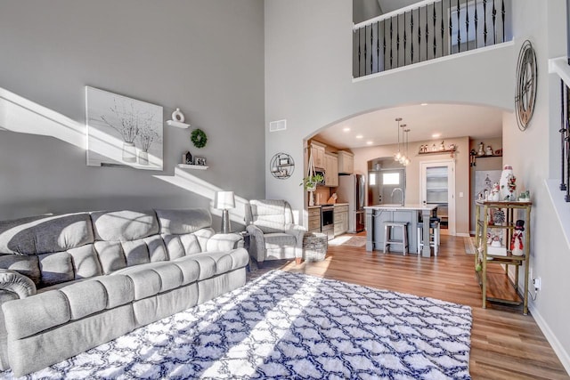 living room with a towering ceiling, light hardwood / wood-style flooring, and sink