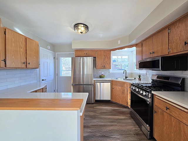 kitchen featuring kitchen peninsula, stainless steel appliances, tasteful backsplash, dark wood-type flooring, and sink