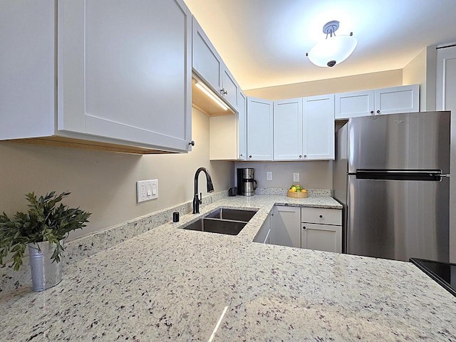 kitchen with white cabinets, stainless steel fridge, light stone counters, and sink