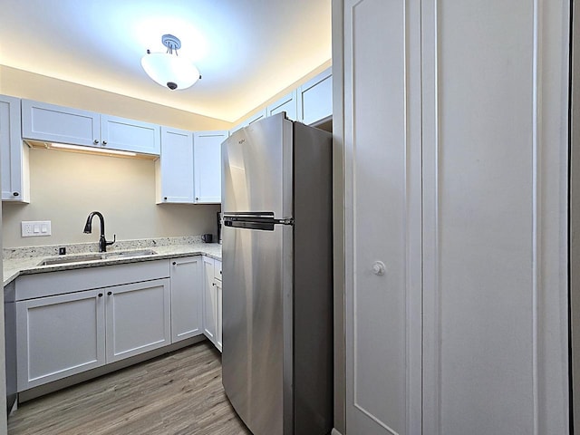 kitchen featuring light hardwood / wood-style floors, stainless steel refrigerator, light stone countertops, white cabinets, and sink