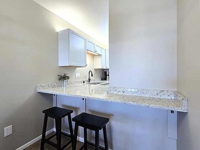 kitchen featuring kitchen peninsula, sink, a breakfast bar area, white cabinets, and light stone counters