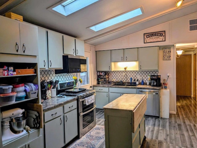 kitchen featuring appliances with stainless steel finishes, a kitchen island, sink, hardwood / wood-style flooring, and lofted ceiling with skylight