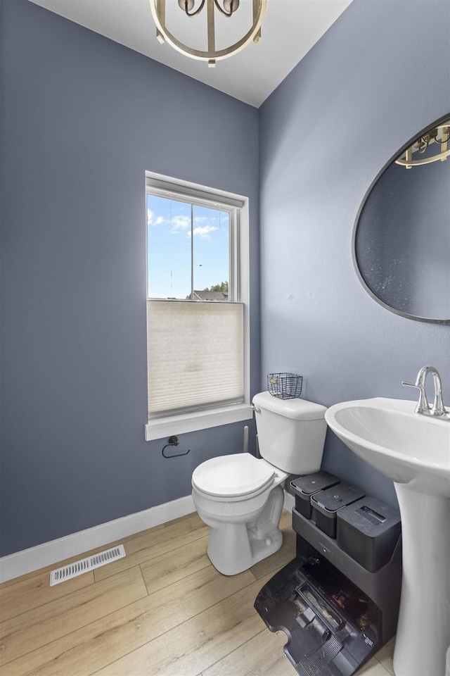 bathroom featuring toilet, an inviting chandelier, hardwood / wood-style floors, and sink