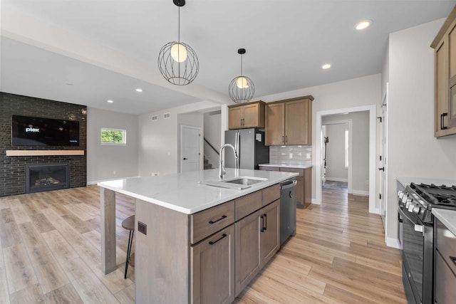 kitchen featuring appliances with stainless steel finishes, a fireplace, decorative backsplash, sink, and an island with sink