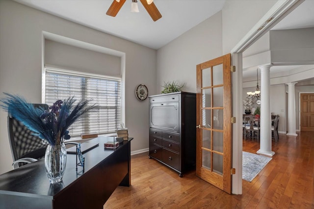 office with light wood-type flooring, ceiling fan with notable chandelier, and ornate columns