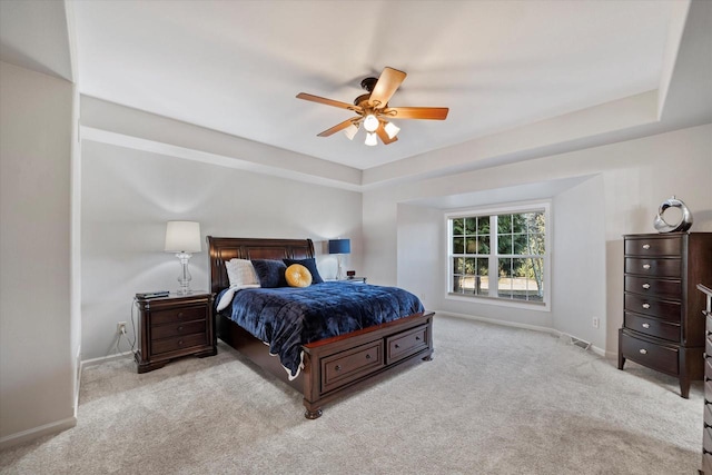 carpeted bedroom with ceiling fan and a raised ceiling