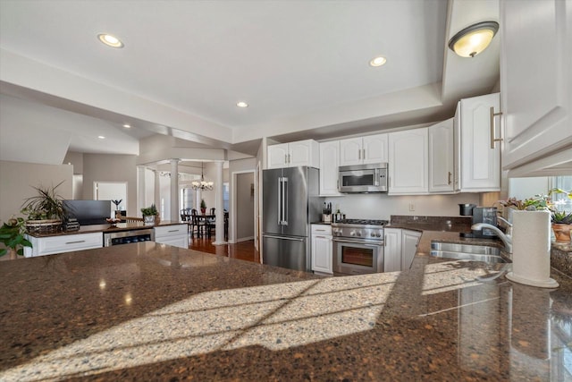 kitchen with white cabinets, dark stone counters, an inviting chandelier, sink, and high quality appliances