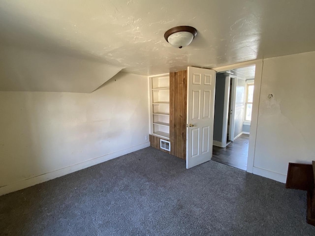 bonus room with dark carpet and vaulted ceiling