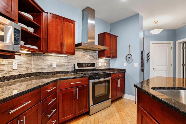 kitchen with decorative light fixtures, backsplash, wall chimney range hood, dark stone countertops, and stainless steel appliances