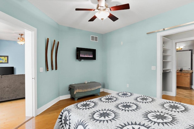 bedroom with a spacious closet, sink, a closet, light wood-type flooring, and ceiling fan