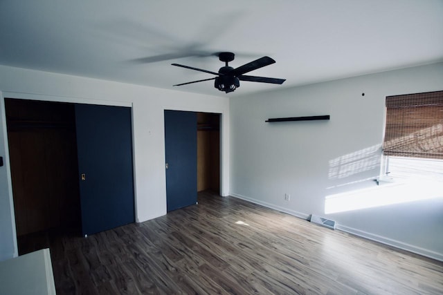 unfurnished bedroom with ceiling fan, multiple closets, and dark hardwood / wood-style floors